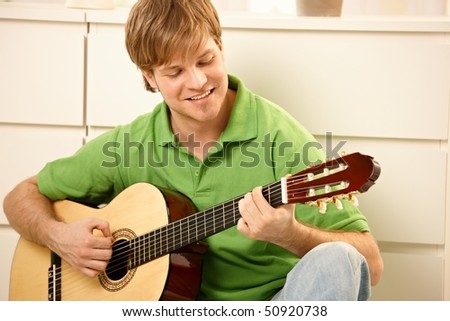 Goodlooking guy playing guitar at home.