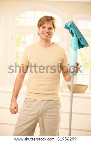 Goodlooking young guy posing with mop in hand at home, smiling at camera.