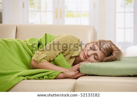 Blond woman sleeping with blanket on couch in sunlit living room at home.