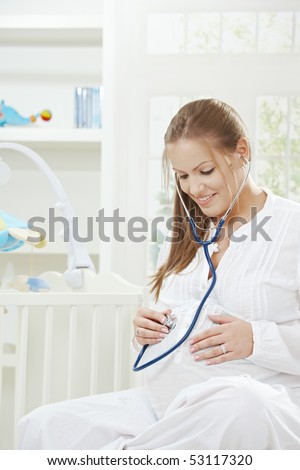 Pregnant woman listening baby's heartbeat with stethoscope placed on her belly.