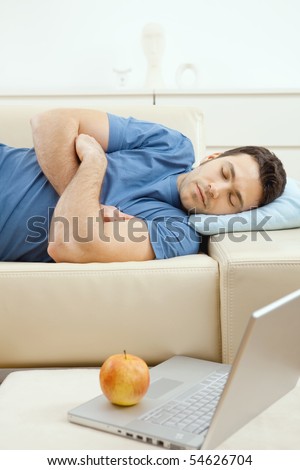 Young handsome man sleeping on couch at home, side view.  Laptop computer on desk.