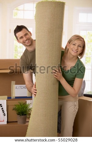 Portrait of smiling couple moving house, holding carpet rolled up, surrounded with boxes.