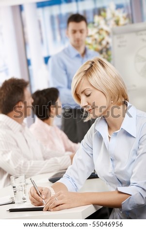 Young businesswoman sitting at table in meeting room writing notes.