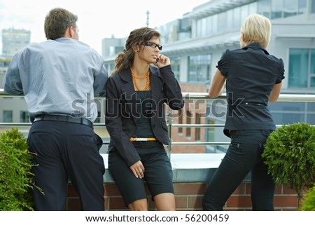 Business people having break on terrace of office building, businesswoman talking on mobile phone.