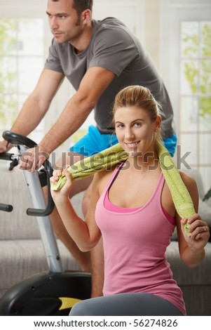 Man training on exercise bike, woman doing streching exercise on fitness mat at home.