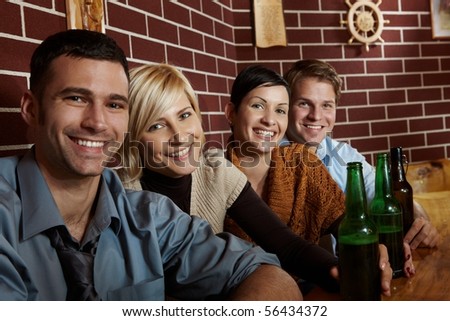 Portrait of happy young people sitting in pub, drinking beer, looking at camera, smiling.