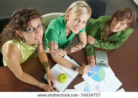 Three young businesswomen sitting at meeting room, discussing financial charts on table. Overhead shot.