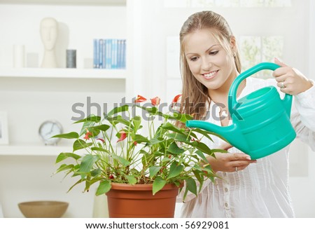 Happy young woman watering plant using sprinkling can, smiling.
