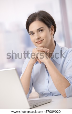 Portrait of mid-adult female office worker smiling at camera sitting with laptop computer.?