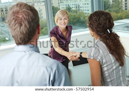 Business people shaking hands over meeting table at office, smiling.