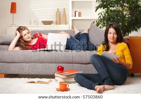 Pretty schoolgirls looking at camera learning together in living room with books and computer?