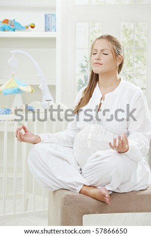 Pregnant woman sitting in yoga position besides new crib in children\'s room.