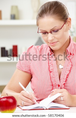Attractive young woman sitting at table writing in diary book.