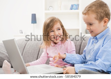 Happy children sitting on couch at home, browsing internet on laptop computer. Girl smiling at boy who looking at screen.
