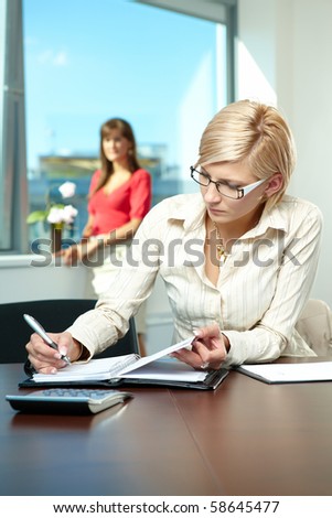 Young businesswoman sitting at desk in office, writing notes to personal organizer.