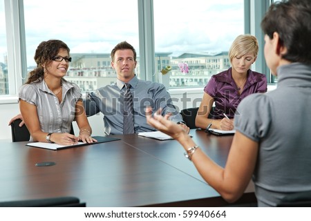 Panel of business people sitting at table in meeting room conducting job interview talking with applicant.