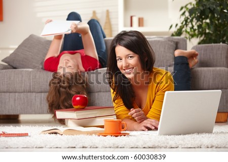 Happy students studying at home in living room with books and laptop, looking at camera smiling.?
