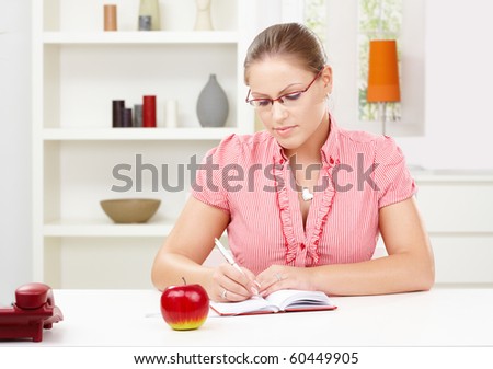 Attractive young woman sitting at table writing in diary book.