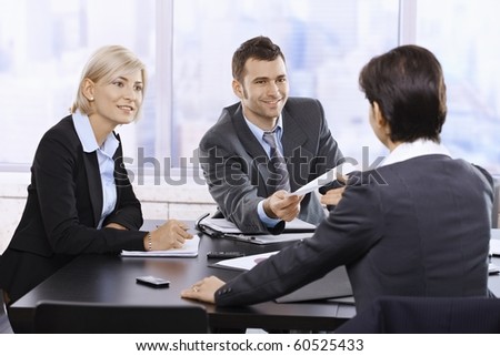Businesspeople smiling at meeting, businessman handing over document sitting at table.?