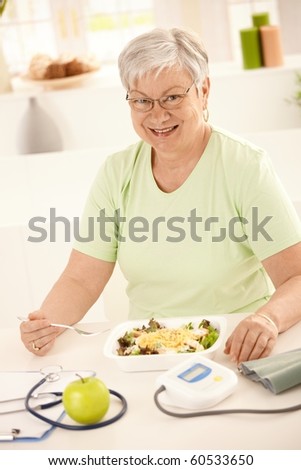 Happy senior woman eating healthy salad at home. Looking at camera, smiling.?