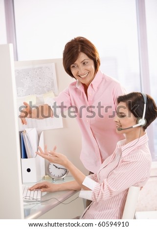 Smiling coworkers discussing work in office, supervisor pointing at customer care operator computer screen.?