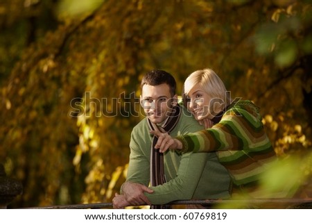 Happy couple on autumn walk in park, woman showing something to man, smiling.?