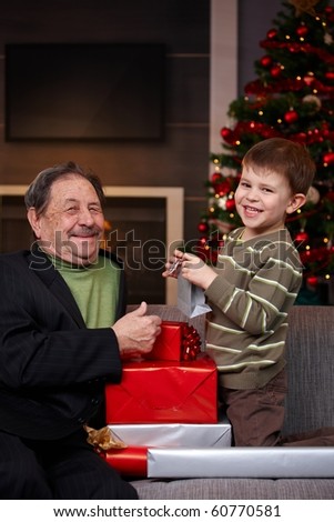 Small boy giving christmas present to happy grandfather, smiling. ?