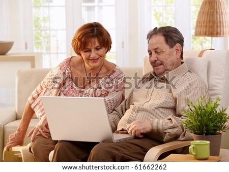 Elderly couple using laptop computer at home, looking at screen, smiling.?