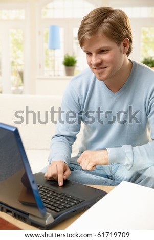 Goodlooking guy using laptop computer, browsing internet at home, smiling.?
