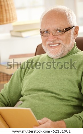 Portrait of smiling senior man wearing glasses, sitting at home holding book.?