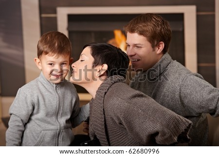 Happy family sitting on couch at home in front of fireplace, looking at camera, smiling.