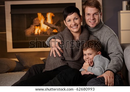 Happy family sitting on couch at home in a cold winter day, looking at camera, smiling.