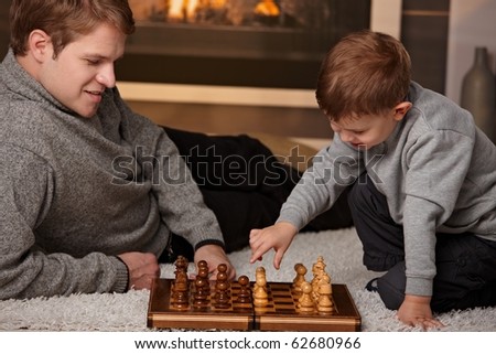 Father and 4 years old son playing chess at home in a cold winter day.