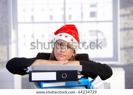Young woman in santa hat sitting in office leaning on folders, having trouble.?
