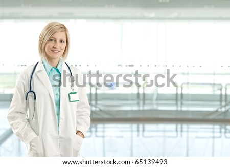 Portrait of attractive female doctor on hospital corridor looking at camera smiling. Copy space on right.?