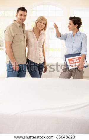 Estate agent showing young happy couple around in new house.?