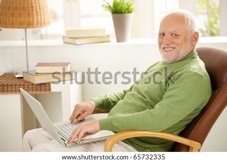 Portrait of aged man sitting in armchair with laptop computer, smiling at camera.?