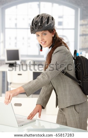 Young attractive businesswoman leaving office by bike, shutting down her laptop, wearing helmet and backpack.?