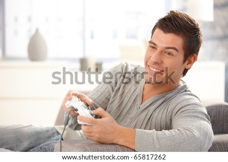 Young guy enjoying computer game, playing with joystick, smiling happily.?