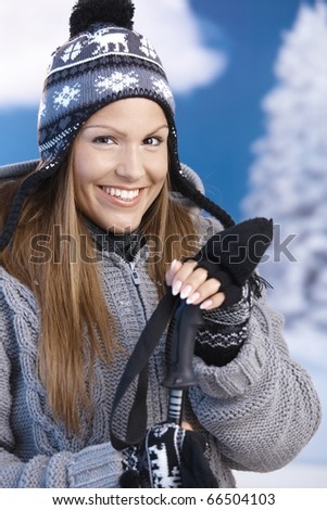 Pretty young girl dressed up warm for skiing wearing cap and gloves smiling front of winter landscape .?