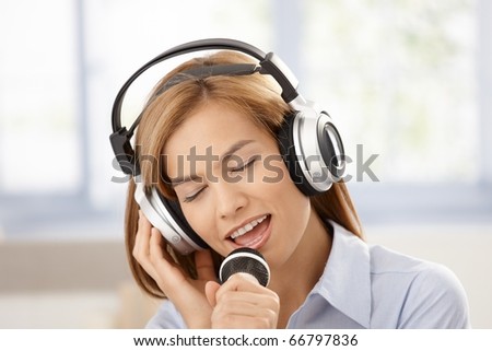 Young attractive female singing with joy, using microphone and headphones, smiling.?