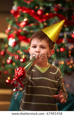 Little boy in new year\'s eve hat blowing horn, looking at camera.