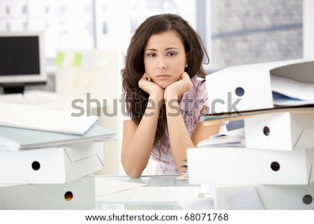 Young office worker sitting troubled in bright office among folders.?