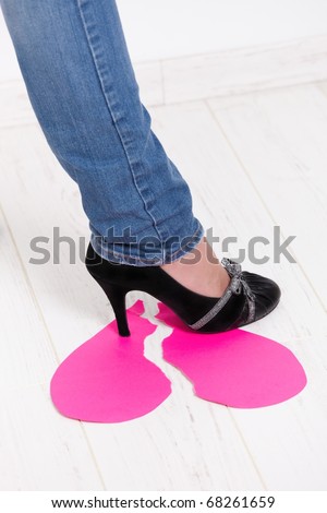 Female leg wearing jeans and high heel shoes treading on torn paper heart.?