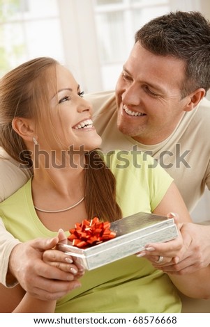 Couple sitting together laughing happily, woman holding present, man holding woman\'s hands.?