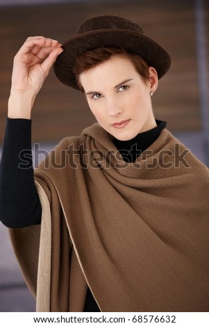 Trendy woman wearing polo-neck top and big beige scarf posing with hat, looking at camera.?
