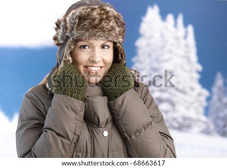 Pretty young girl dressed up warm in coat, fur-hat and gloves, smiling front of winter landscape.?