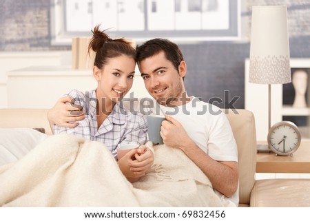 Young couple drinking tea in bed, hugging each other, smiling happily.?