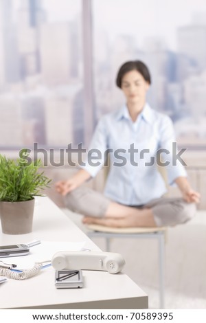 Not answering phone in skyscraper office, female office worker doing yoga meditation in background.?