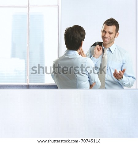 Two coworkers standing chatting in business office, smiling.